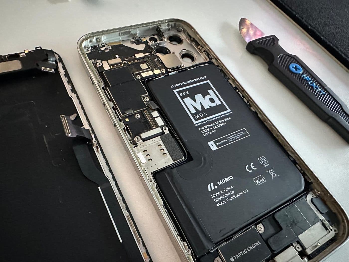 An iPhone opened on a white bench beside its battery and a repair tool